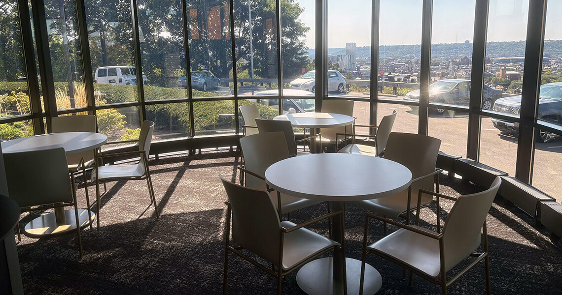Three white tables in a room with a curved wall of windows looking out at Downtown Cincinnati