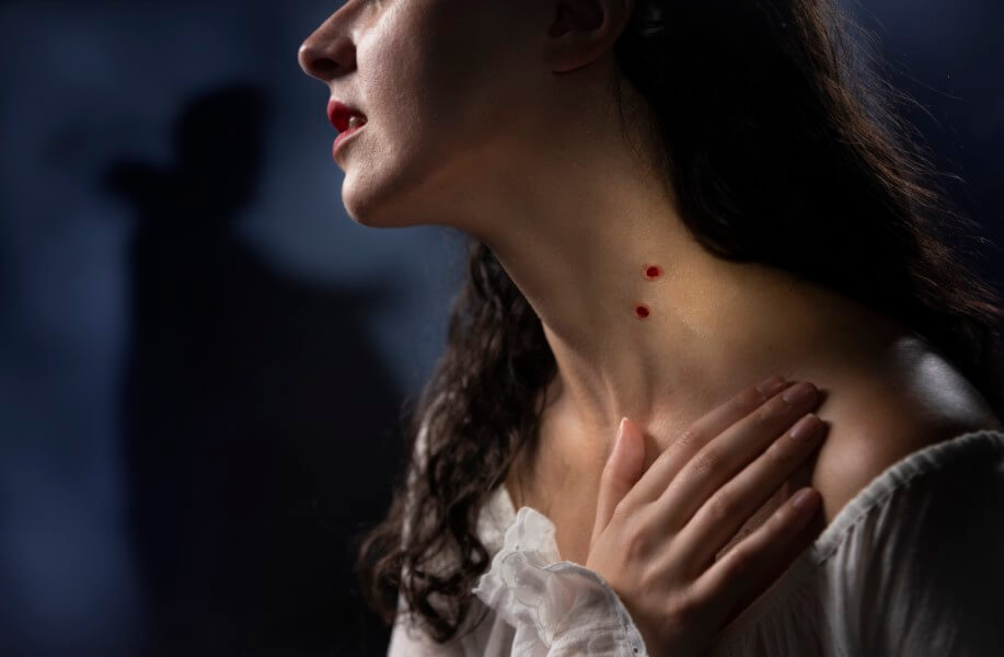 White young woman in white with vampire bite on neck and looming shadow in the background