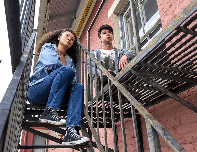 Young mixed-race couple sitting on fire escape of a red brick building.