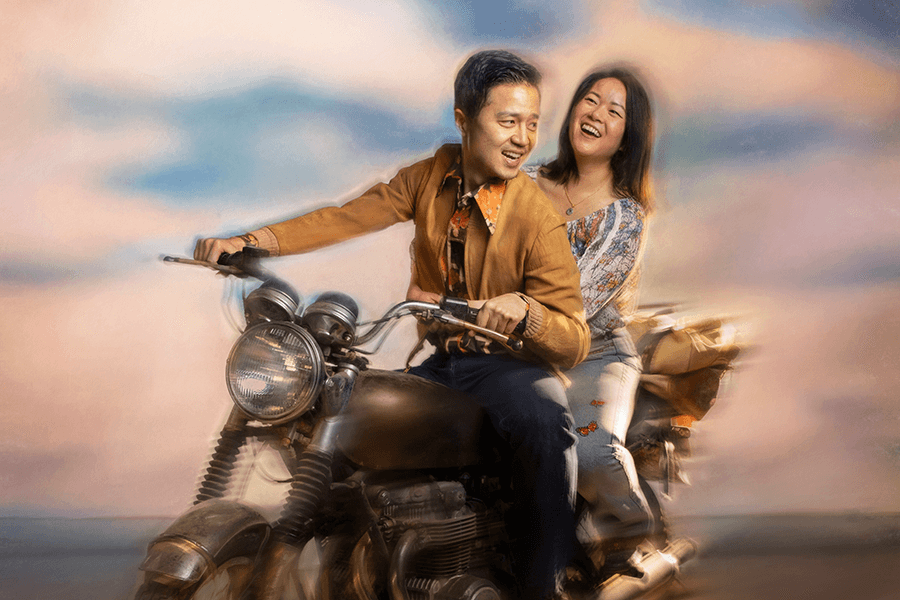 Young asian couple on a laden motorcycle moving quickly with an open cloudy sky.